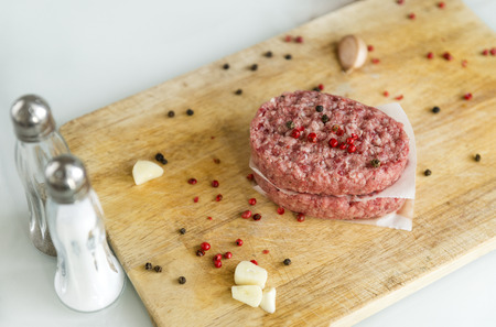 2 beef raw cutlets on wooden Board with spices, meat, garlic, pepper, salt in salt shaker, raw food...