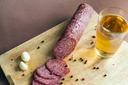 smoked sausage cut on a wooden chopping Board  garlic and a glass of beer, with pepper,の写真素材