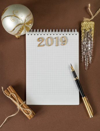 clean Notepad sheet, lettering 2019,  fountain pen, writing space, Christmas ball, artificial transparent icicle, cinnamon sticks on brown background, top view, flat layの写真素材