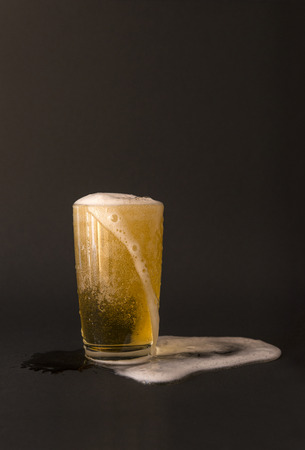 glass of light beer with foam on a black background