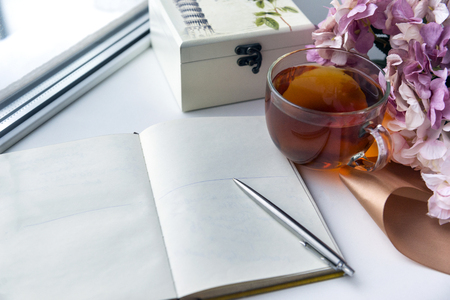open Notepad with a clean sheet of paper, a mug of black tea, silver pen , jewelry box, hydrangea flowers near the window, place the milking inscriptionsの写真素材