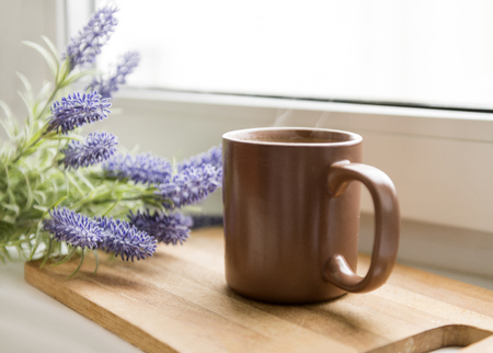 mug with a hot drink, a sprig of blue lavender on the windowsillの写真素材