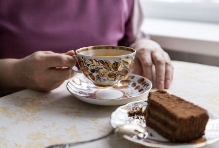 Cup of tea in womens hands, a piece of chocolate cake on a plate, tea, drink