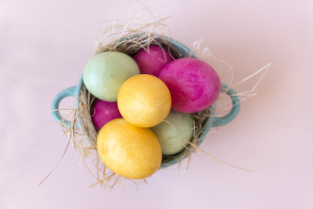 pink , yellow, green Easter eggs in a plate on a beige background, top view