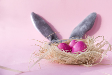 3 pink Easter eggs in nest, grey Bunny ears on pink backgroundの写真素材
