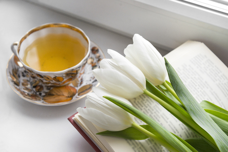 mug of tea, 3 white tulips on the book near the windowの写真素材