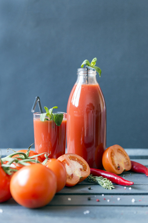 tomato juice, juice in a glass, tomato juice in a bottle, tsetye tomatoes, pepper, mint, rosemary on a gray backgroundの写真素材