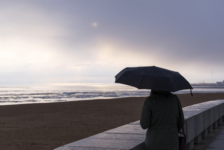 man with a black umbrella looks at the beach and the Gulf of Finland on a rainy day in springの写真素材