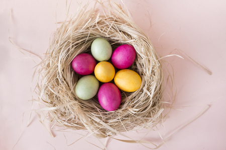 pink, yellow , green Easter eggs in nest on beige background, top view,の写真素材