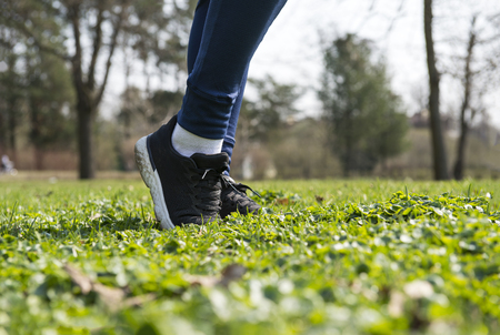 women's feet in black sneakers and leggings on the grass on the lawn on a Sunny day , sports shoesの写真素材