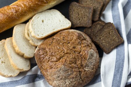 loaf, pieces of bread, wheat and rye bread on towel on dark background,