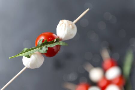 mozzarella balls with cherry tomatoes and a sprig of arugula on a wooden Spaska, canape  on a dark...