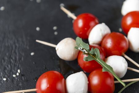 mozzarella balls with cherry tomatoes on skewers, arugula leaf with sesame seeds, canapes on a black background, cheese with vegetablesの写真素材