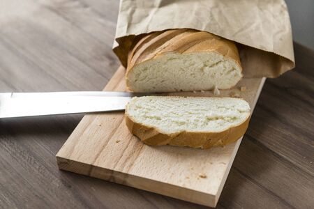 cut piece of bread on cutting Board, knife, loaf on brown background