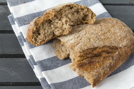 broken in half loaf of fresh rye bread on a striped towel on a gray wooden background, 2 pieces of breadの写真素材