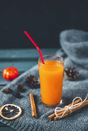 1 Cup orange vegetable pumpkin juice with a straw, cinnamon, cones, cinnamon, a slice of dried orange on a dark backgroundの写真素材
