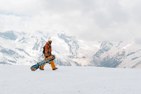 man, snowboarder with a snowboard in hand is on the snow in the mountains, Caucasus, athleteの写真素材