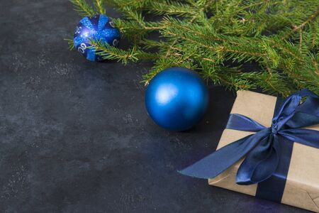 fir branches, blue balls, gift box with blue ribbon on black background, Christmas decor, place for...