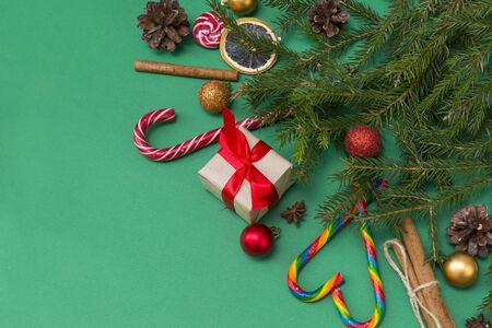 fir branches on a green background, a gift box with a red ribbon, cones, Golden and red balls, cinnamon sticks, candy, top viewの写真素材