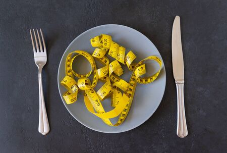 yellow measuring tape, measuring tape on a gray plate, knife, fork on a black background, dietの写真素材