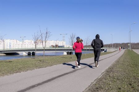 2 people running down the street in the city along the river embankment on the background of...