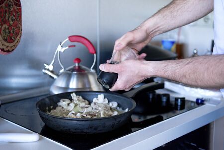 man adds spices to fried mushrooms in pan on kitchen stove cooking, home food,の写真素材