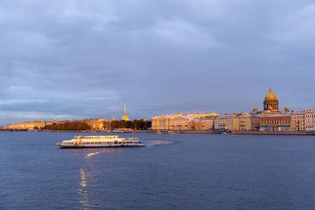 pleasure boat on the Neva river at sunset, nabrezhnaya with buildings and the dome of St. Isaac's...