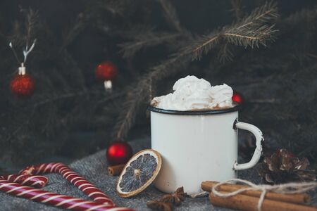 1 mug hot chocolate with whipped cream, lollipops, fir branches, red balls, cinnamon, dried orange slice on dark background, winter Christmas hot drinkの写真素材