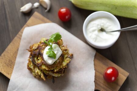 zucchini pancakes with sour cream and herbs on a Board, cherry tomatoes, garlic, , fresh raw zucchini,  top viewの写真素材