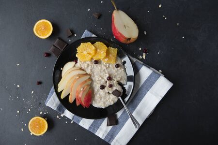 1 plate of oatmeal with slices of pear, orange, cranberries and chocolate on a black backgroundの写真素材