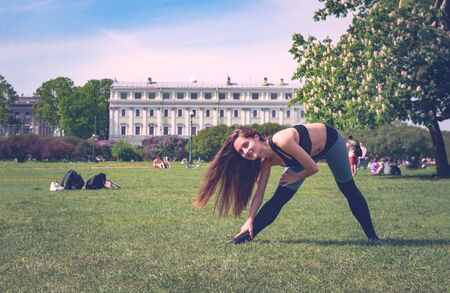 1 white young slender woman doing yoga in the Park on a Sunny day, the girl doing leans forwardの写真素材
