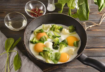 fried eggs with broccoli and spinach in a pan on a wooden background