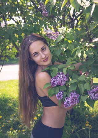 portrait of a 1 white  beautiful slender brown haired girl with long hair near a lilac Bushの写真素材