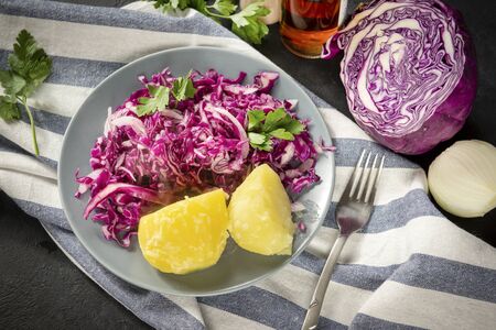 1 plate of red cabbage vegetable salad with parsley and boiled potatoes, fork on a towel on a black...