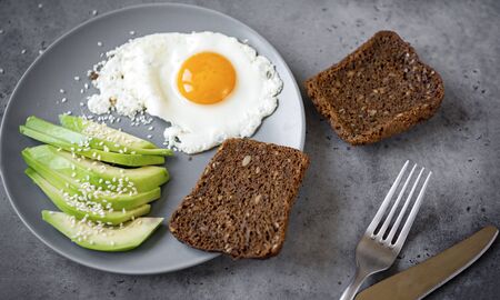 eggs with avocado with slices of grain bread on a plate on a gray background, forkの写真素材