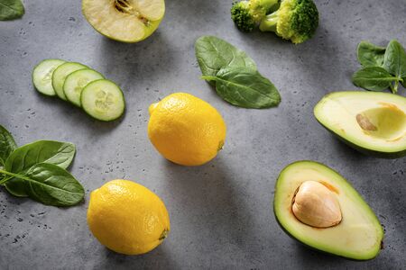 Apple, half  avocado halves with a stone,  broccoli, fresh green spinach leaves, yellow lemon, cucumber slices  a blank sheet of Notepad on a gray background,  top view,  flat layの写真素材