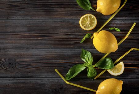 3 whole yellow juicy lemons, Basil, cocktail tubes on a dark wooden background, citrus, top view, copy space, flat layの写真素材