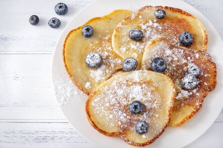 fried pancakes with fresh blueberries with powdered sugar on a plate, close up, top view