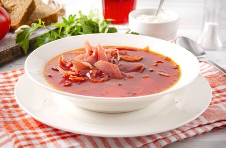 1 plate of borscht, Ukrainian soup with beetroot in a white plate on a checked towel, greens,