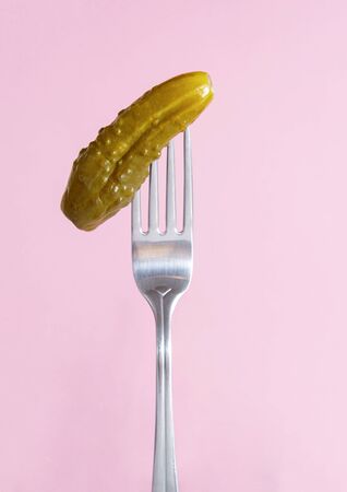 1  pickled cucumber with a fork on a pink  background, vegetablesの写真素材