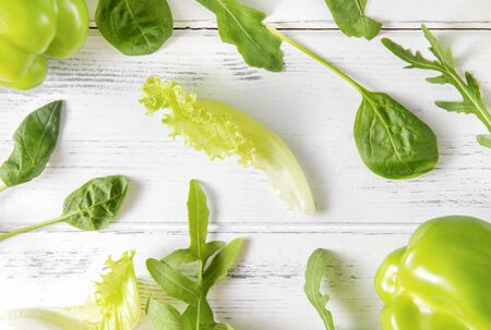 green sprigs of lettuce, pepper,  fresh spinach, arugula  on a white wooden background