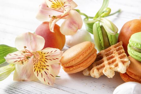 peach, green macaroon cookies with yellow Alstroemeria flowers, fresh apricots, waffle on a beige backgroundの写真素材