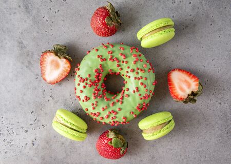 1 donut with green icing, macaroon  and red strawberries on a gray background top view, sweetsの写真素材
