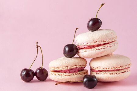 3 beige French macaroons with cherries with pink cream on a pink background, cookiesの写真素材
