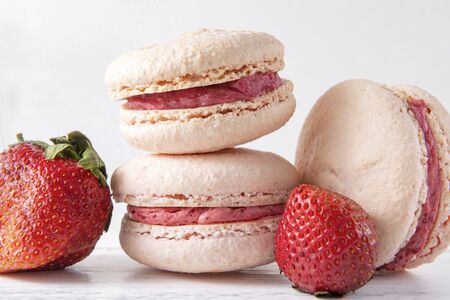 beige French macaroons   with strawberry  pink cream on a white wooden background, 3 cookiesの写真素材