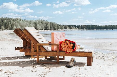 wooden deck chairs on the beach on a Sunny day, sandy beach, bouquet of roses, bag, shoes, Gulf of...