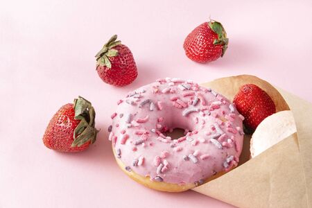 1 donut with pink icing, fresh strawberries in an envelope on a pink backgroundの写真素材