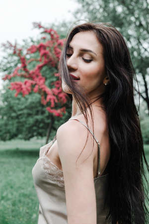 1 beautiful stylish brunette woman with long hair in a beige top against the background of flowering trees in the Parkの写真素材