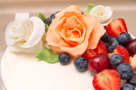 cake with white mastic decorated with beige roses from mastic and fresh berries, blueberries,...