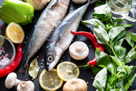 2 raw mackerel fish with lemon slices, Basil, chili pepper, mushrooms, salt and spices on a black...